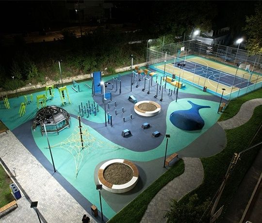 Beleuchteter urbaner Sportpark mit Fitnessgeräten und Basketballfeld